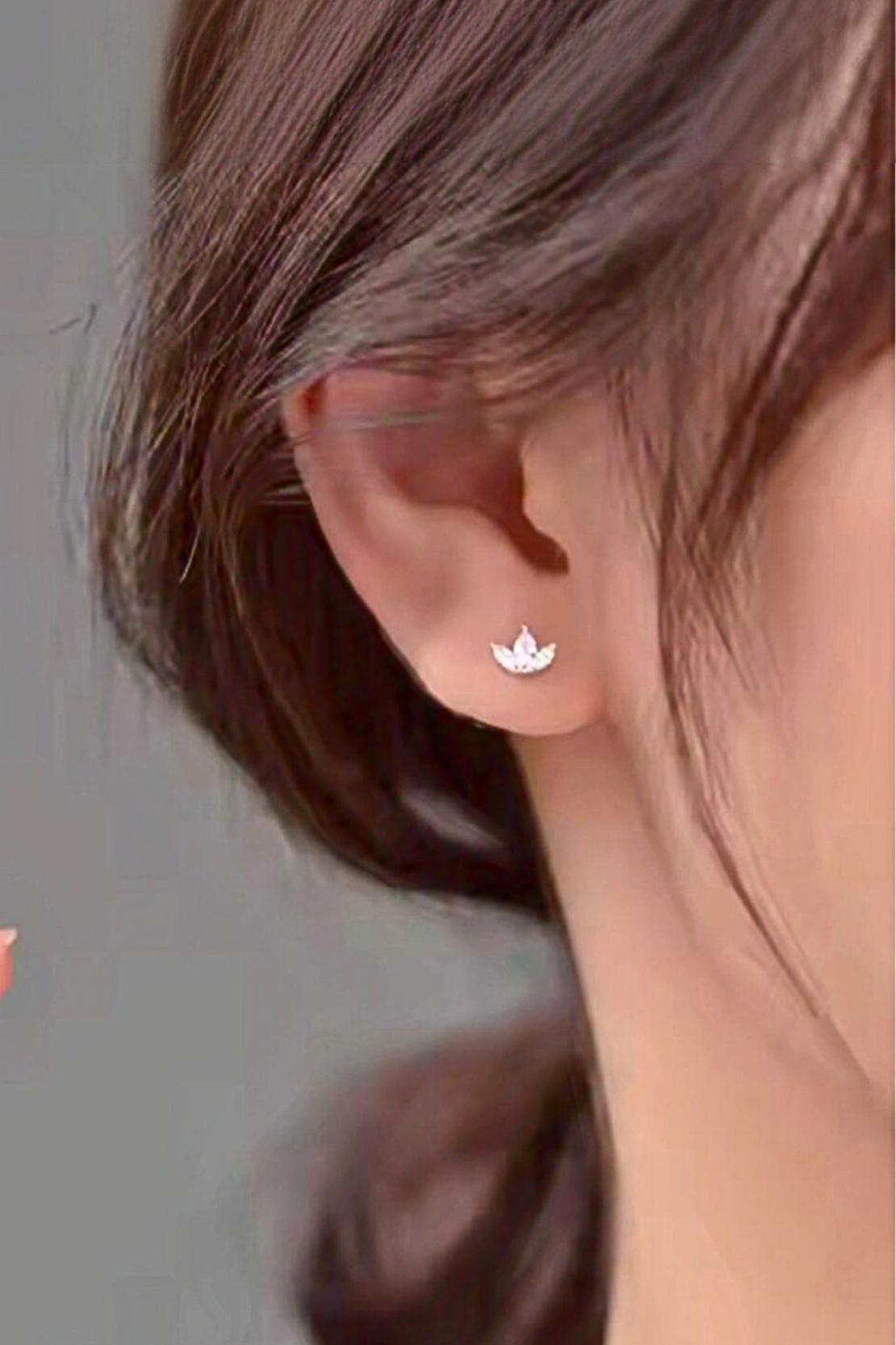 Close-up of an ear wearing a small silver earring with a floral design.
